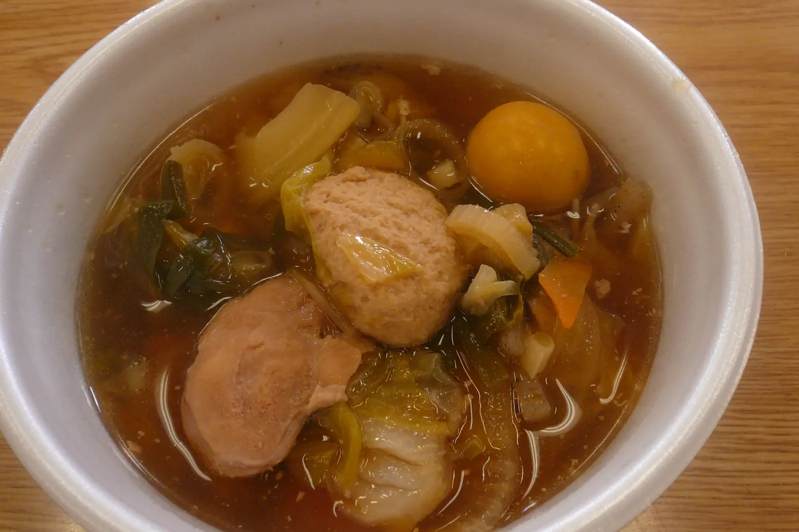 Una ciotola bianca di stufato chankonabe con una polpetta di pesce, un tuorlo d'uovo, cavolo e carota in un brodo scuro, su un tavolo di legno